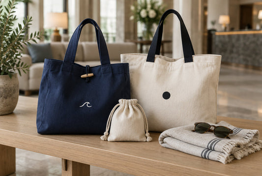 Luxury travel gift bags: a French navy canvas tote and a natural cotton shopper with a small drawstring pouch in a hotel lobby