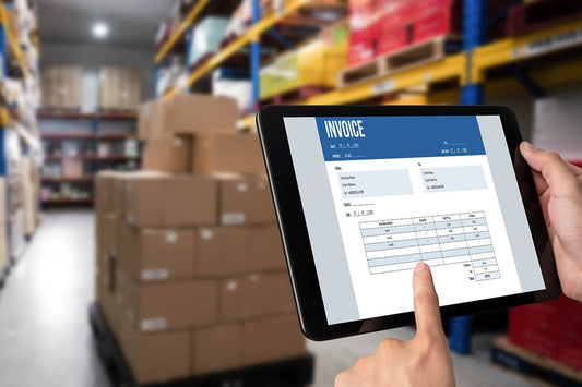 Warehouse worker reviewing a VAT invoice on a tablet beside palletised stock