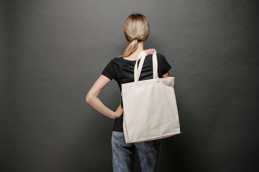 Natural cotton tote bag carried on the shoulder against a dark grey background, used as a corporate gift