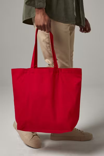 Person carrying a red organic cotton maxi tote with gusset by its long handles