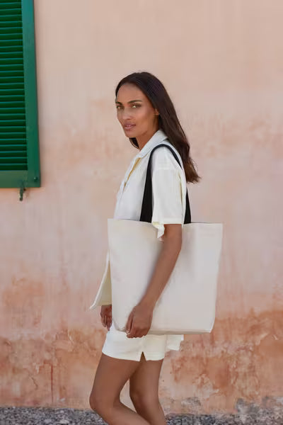 Woman carrying a natural Fairtrade cotton Camden shopper with black handles over the shoulder